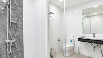 Un baño moderno con cabina de ducha de vidrio, inodoro blanco y lavamanos con espejo superior.