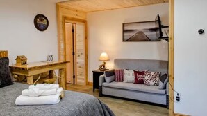 Una habitación acogedora con una cama, un escritorio de madera, un sofá gris y una lámpara.