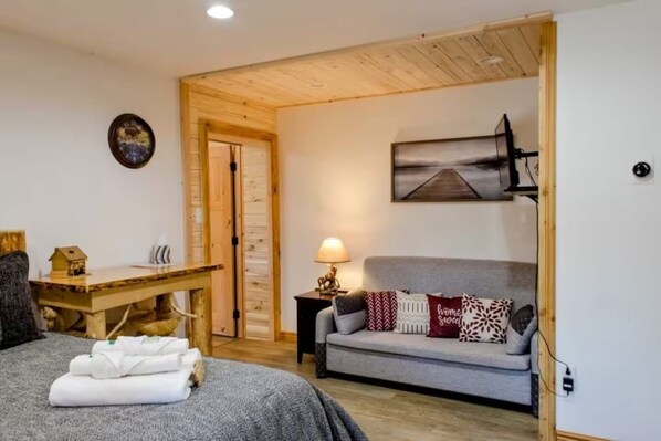 Una habitación acogedora con una cama, un escritorio de madera, un sofá gris y una lámpara.