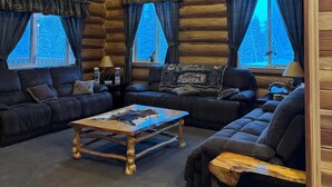 Een chaletinterieur met houten plafond, een zithoek, een salontafel en gordijnen voor de ramen.