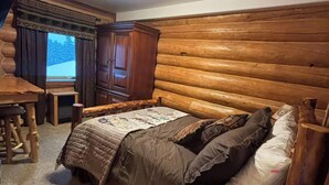 Ein Blockhauszimmer mit einem Bett, einem Holztisch und einem Fenster mit Vorhängen.