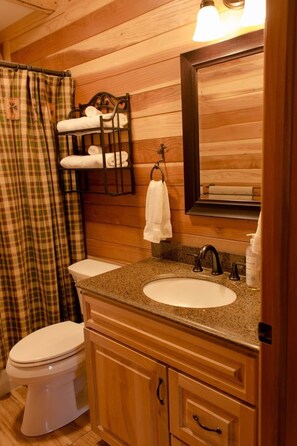 Baño de cabaña de madera con inodoro, lavamanos y perchero para toallas.