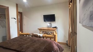 Un dormitorio con una cama, un televisor sobre un mueble de madera y una cortina en la ventana.