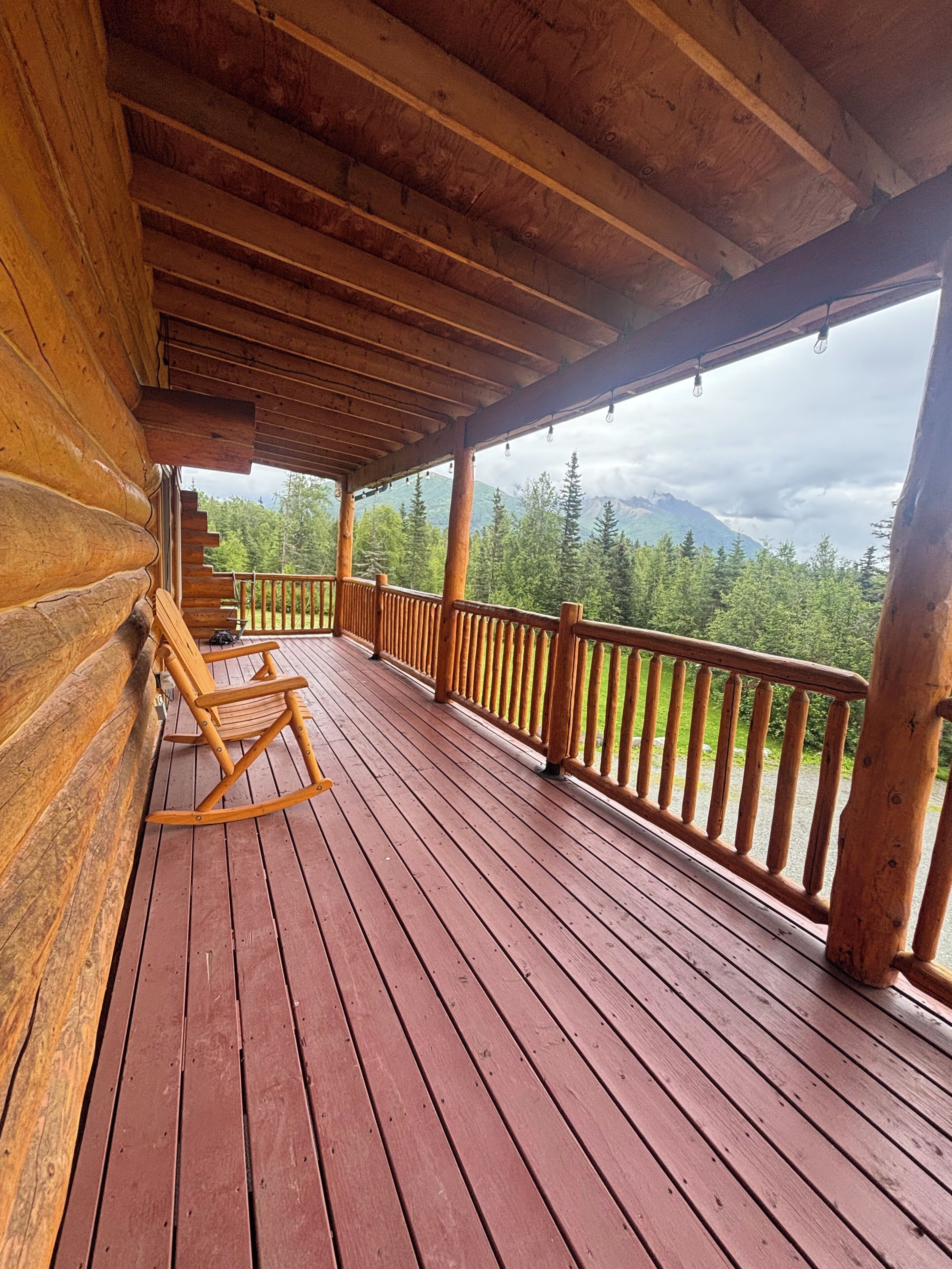 Une terrasse en bois avec un fauteuil à bascule, des rampes en bois et une vue sur une chaîne de montagnes boisée.