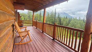 Une terrasse en bois avec un fauteuil à bascule, des rampes en bois et une vue sur une chaîne de montagnes boisée.