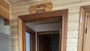 A hallway with wooden walls and a door labeled "Cowboy Barbecue". - Cowboy's Corral~En-Suite Bathroom~Cozy 1 Queen Bed@ Alaska Knotty Pine B&B (Lazy Mountain)