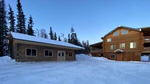 En stuga byggd av trä med ett snötäckt tak, omgiven av ett snöigt landskap och höga träd.
