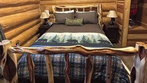 Het interieur van een blokhut met een bed, twee nachtkastjes en een houten hoofdeinde.