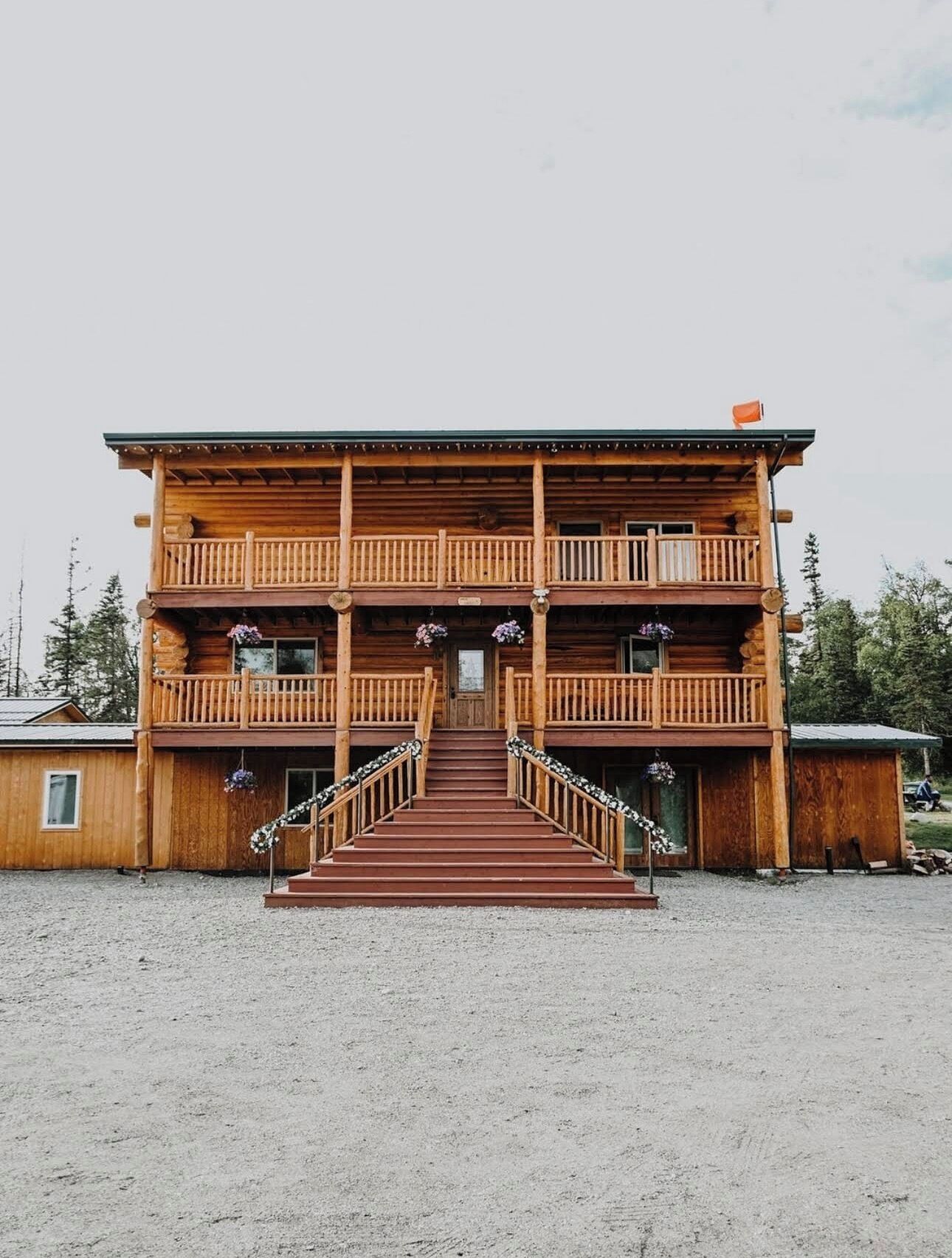 Un chalet en bois à deux étages, doté d’un escalier central menant à la porte d’entrée, et entouré d’une zone recouverte de gravier.