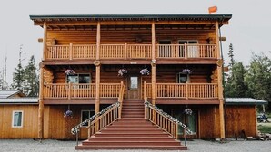 A two-story wooden lodge with a central staircase leading to a front door, surrounded by a gravel area. - Mountain View Suite~Jetted Tub~Private Balcony~3 Beds@ Alaska Knotty Pine B&B (Lazy Mountain)