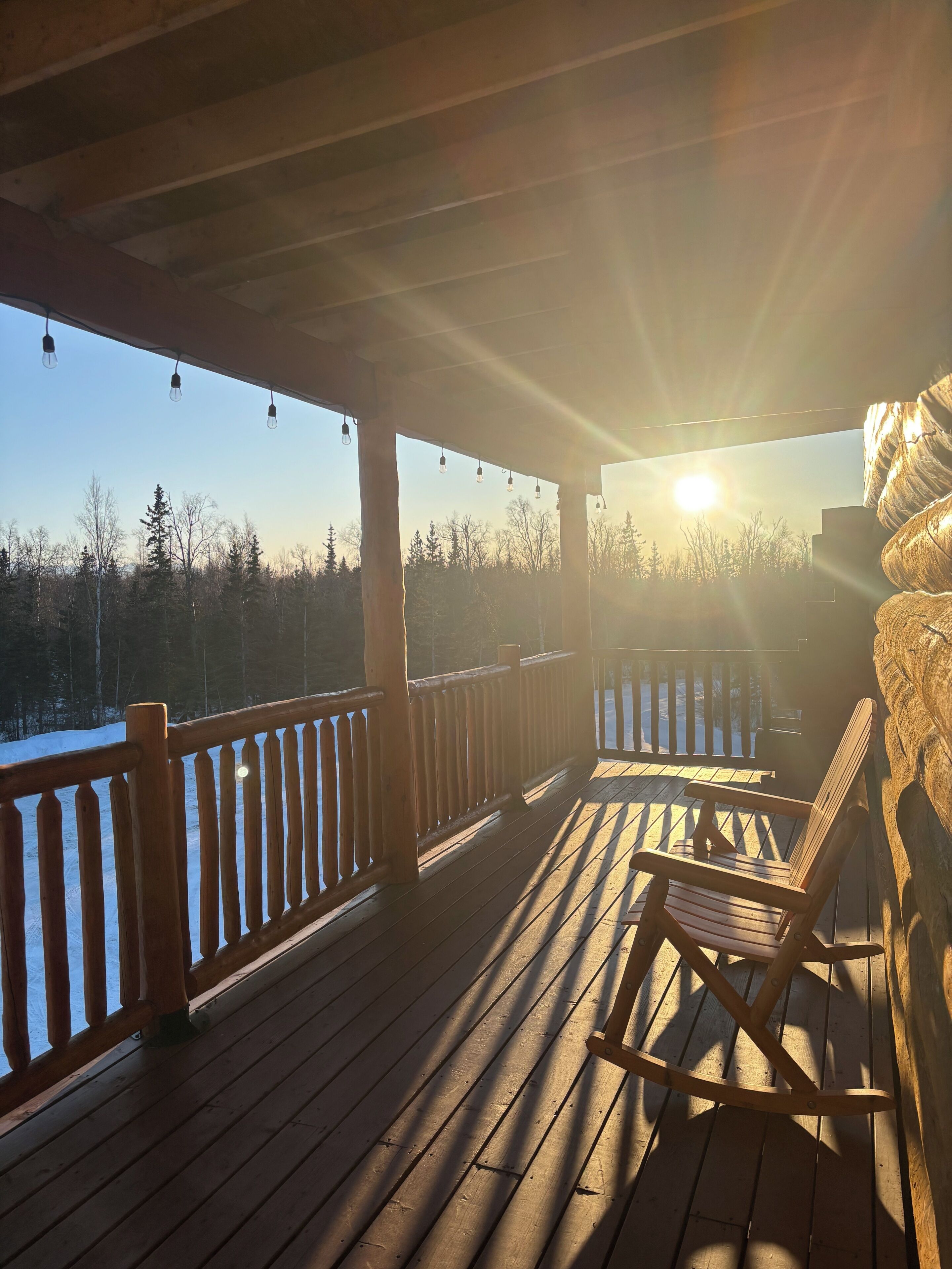 Une terrasse en bois dotée d’une rambarde, d’un banc et offrant une vue sur un paysage enneigé parsemé d’arbres.