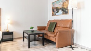 A modern living room with a brown leather sofa, a small table with a plant, a framed picture on the wall, and a floor lamp. - Beautiful 2BR Apt Near Meidling Station (Vienna)