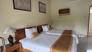 A double bed with white and brown bedding, a wooden nightstand with a lamp, and two framed artworks on the wall. - Raka Rai Bungalow (Ubud)