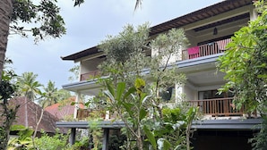 A two-story building with balconies, surrounded by lush greenery and palm trees. - Raka Rai Bungalow (Ubud)