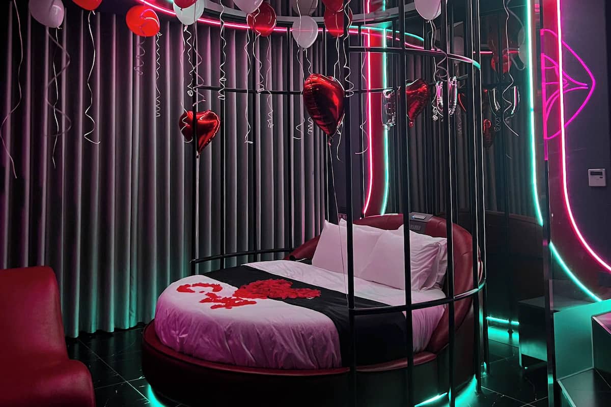 A circular bed with a neon-lit ceiling, a red chair, and a bed with rose petals.
