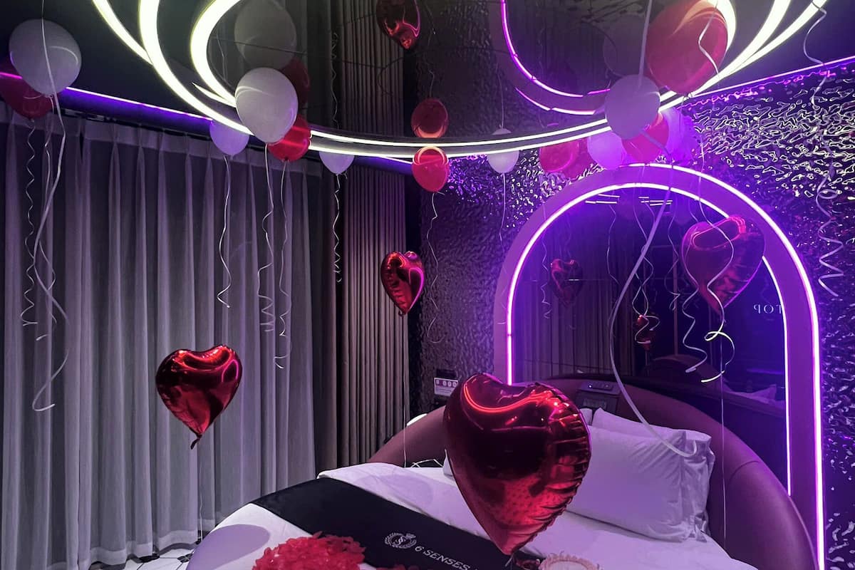 A bedroom with a bed, a neon-lit ceiling, and heart-shaped balloons.