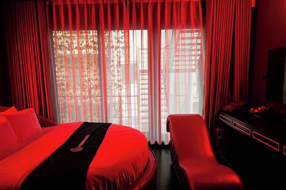 A hotel room with a bed, a chair, a desk, and a view through sheer curtains.