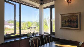 A dining area with a table and chairs, large windows with a view of greenery and buildings, and a wall-mounted light fixture.