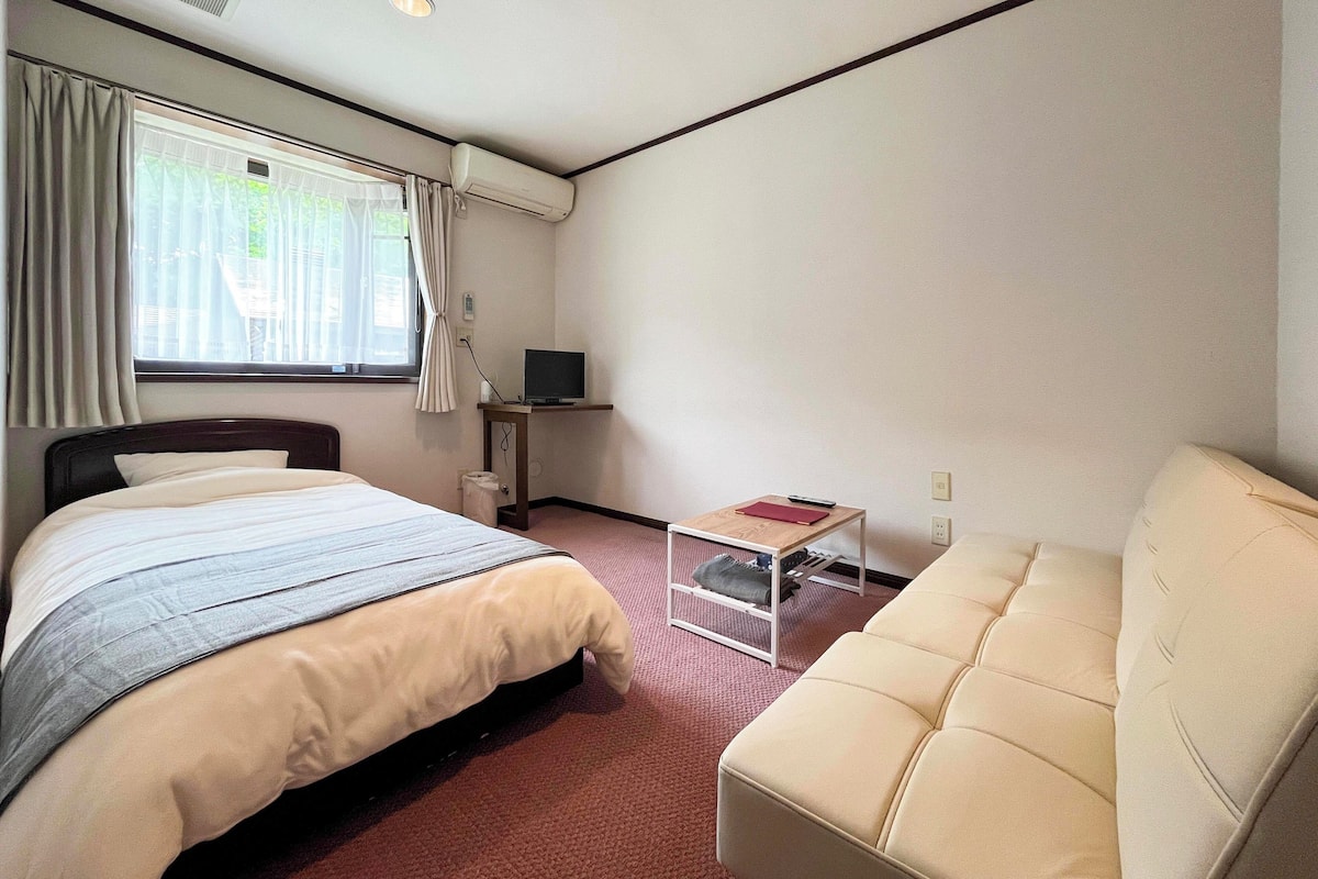 A hotel room with a bed, a TV on a stand, a small table, and a sofa.