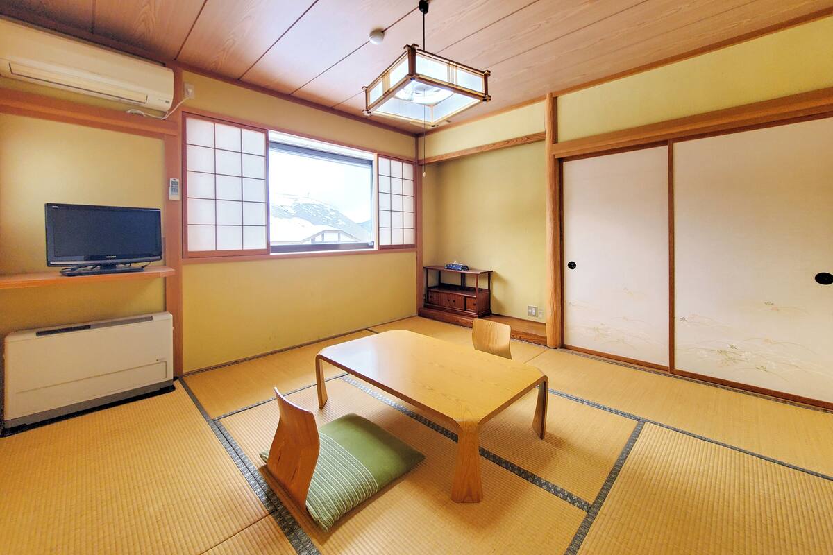 A traditional Japanese room with tatami flooring, a low table, a television, and sliding doors.