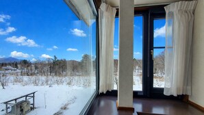 A room with a large window, a door, and a view of a snowy landscape. - Pension HONOBONO (Kitashiobara)