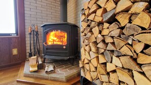 A wood-burning stove with a fire, a stack of firewood, and a brick wall. - Pension HONOBONO (Kitashiobara)