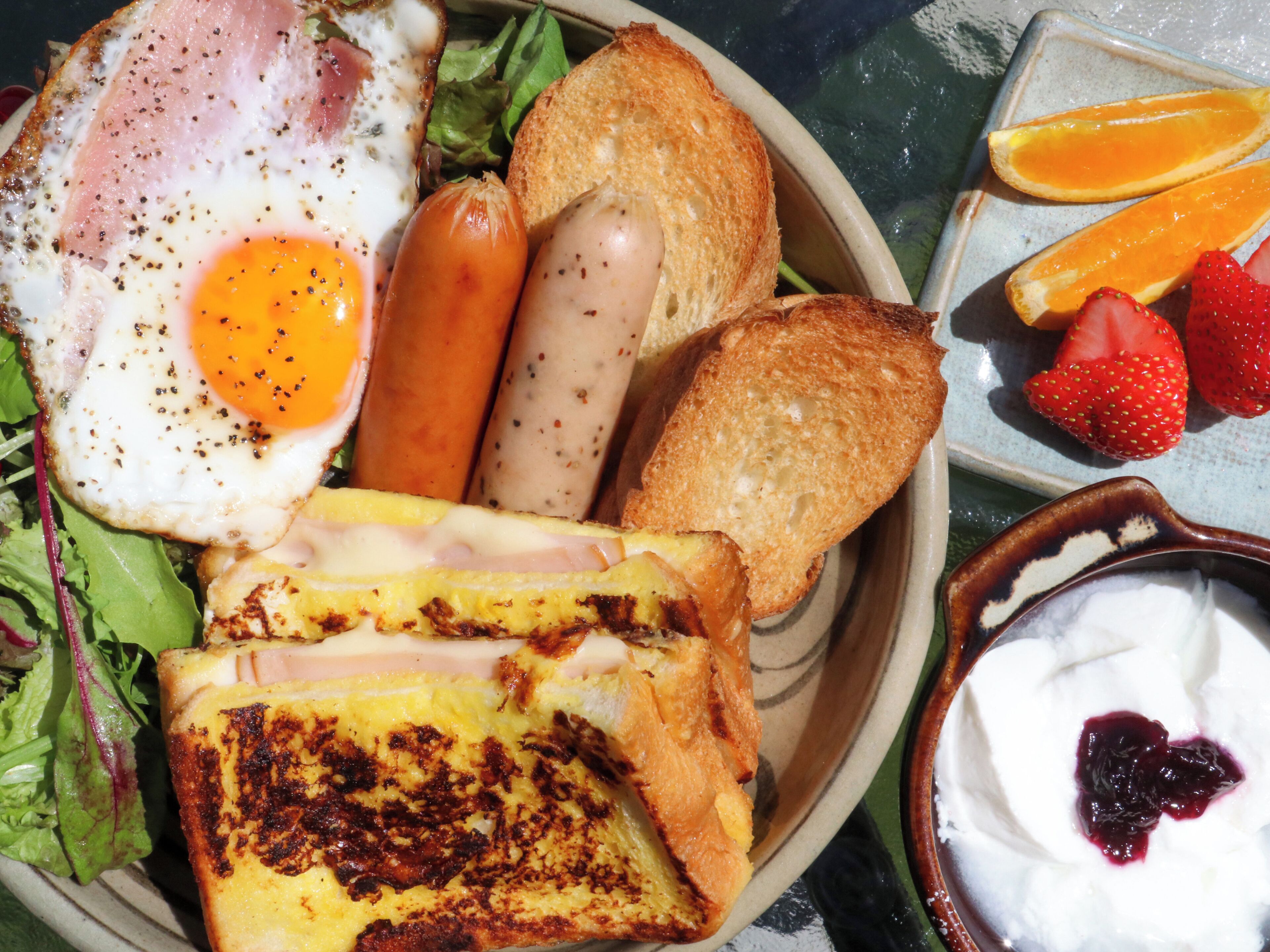 Un plato de desayuno con huevos, salchichas, tostadas, fresas y un tazón de yogur.
