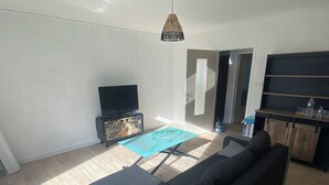 A modern living room with a sectional sofa, a flat-screen TV, a coffee table, and a ceiling light fixture.