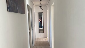 A hallway with wooden flooring, white walls, and a ceiling light fixture.
