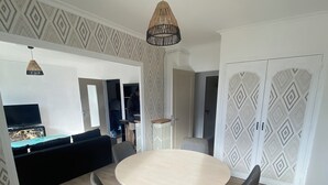 A dining area with a round table and four chairs, a television in the background, and patterned wallpaper.