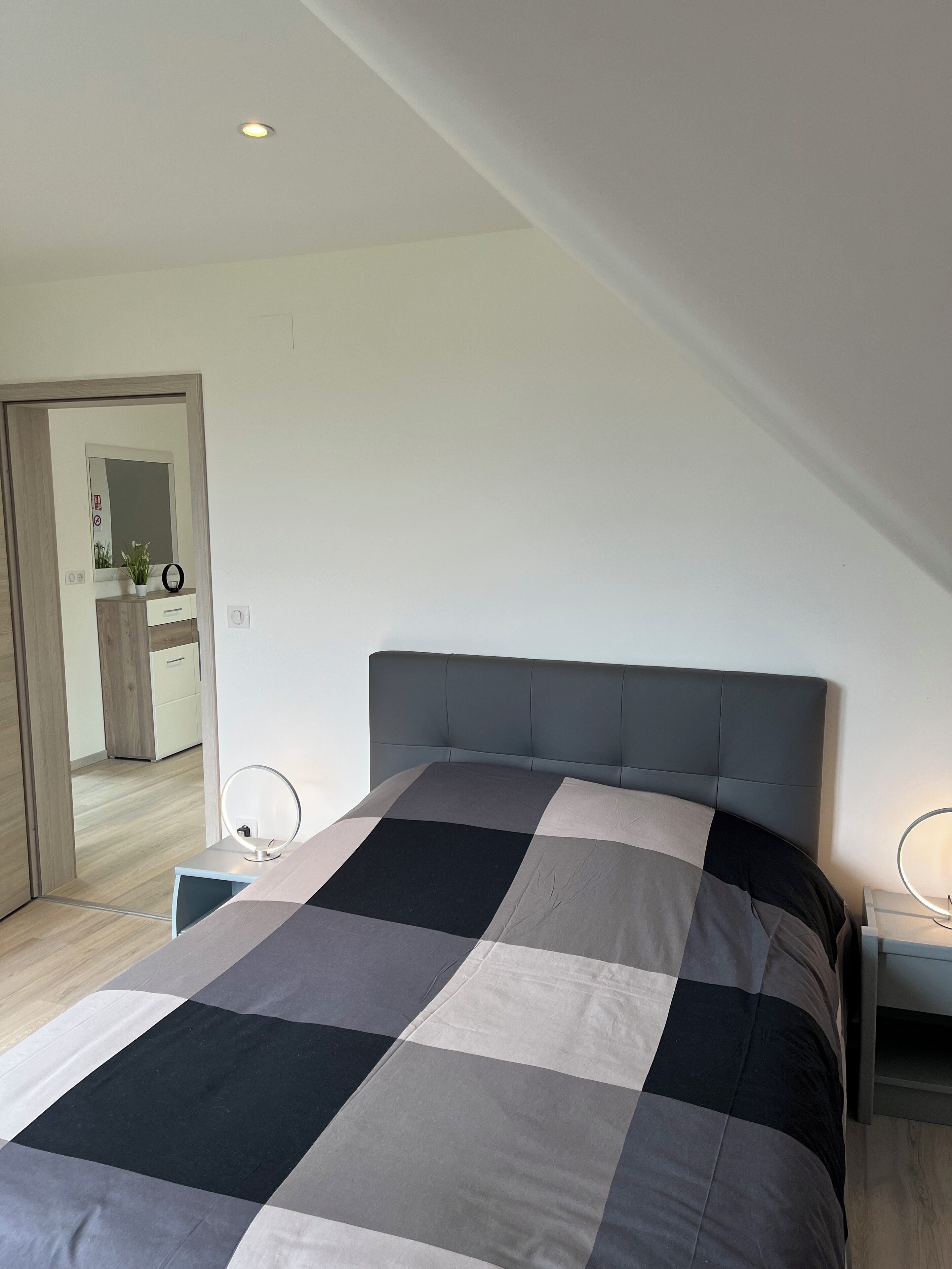 Ein modernes Schlafzimmer mit einem großen Bett, einem Nachttisch mit Lampe und einem Spiegel.
