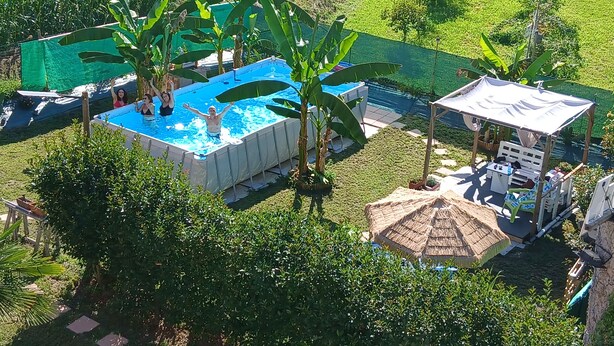 An aerial view of a swimming pool surrounded by lush greenery, a covered seating area, and a thatched-roof structure. - At 9 minutes from Milan Malpensa I rent bed with breakfast, pets allowed (Oleggio)