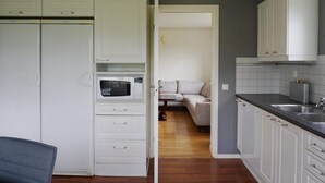 A compact kitchen with white cabinets, a microwave, and a sink. A sofa is visible in the adjacent living area. - 8 Person Holiday Home in Adelso (Adelso)