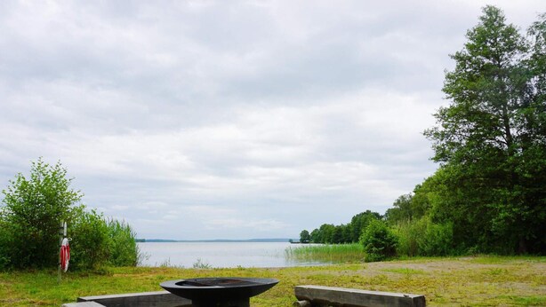 A lakeside campsite with a fire pit, benches, and a walking path. - 8 Person Holiday Home in Adelso (Adelso)
