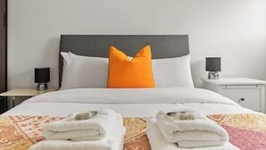 A hotel room with a bed, a nightstand, and a wall-mounted lamp. - New! Spacious 3BR Flat in East London,7min to Tube (Greater London)