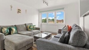 A living room with a grey sofa set, a coffee table, and a view of the outdoors through large windows. - New! Spacious 3BR Flat in East London,7min to Tube (Greater London)