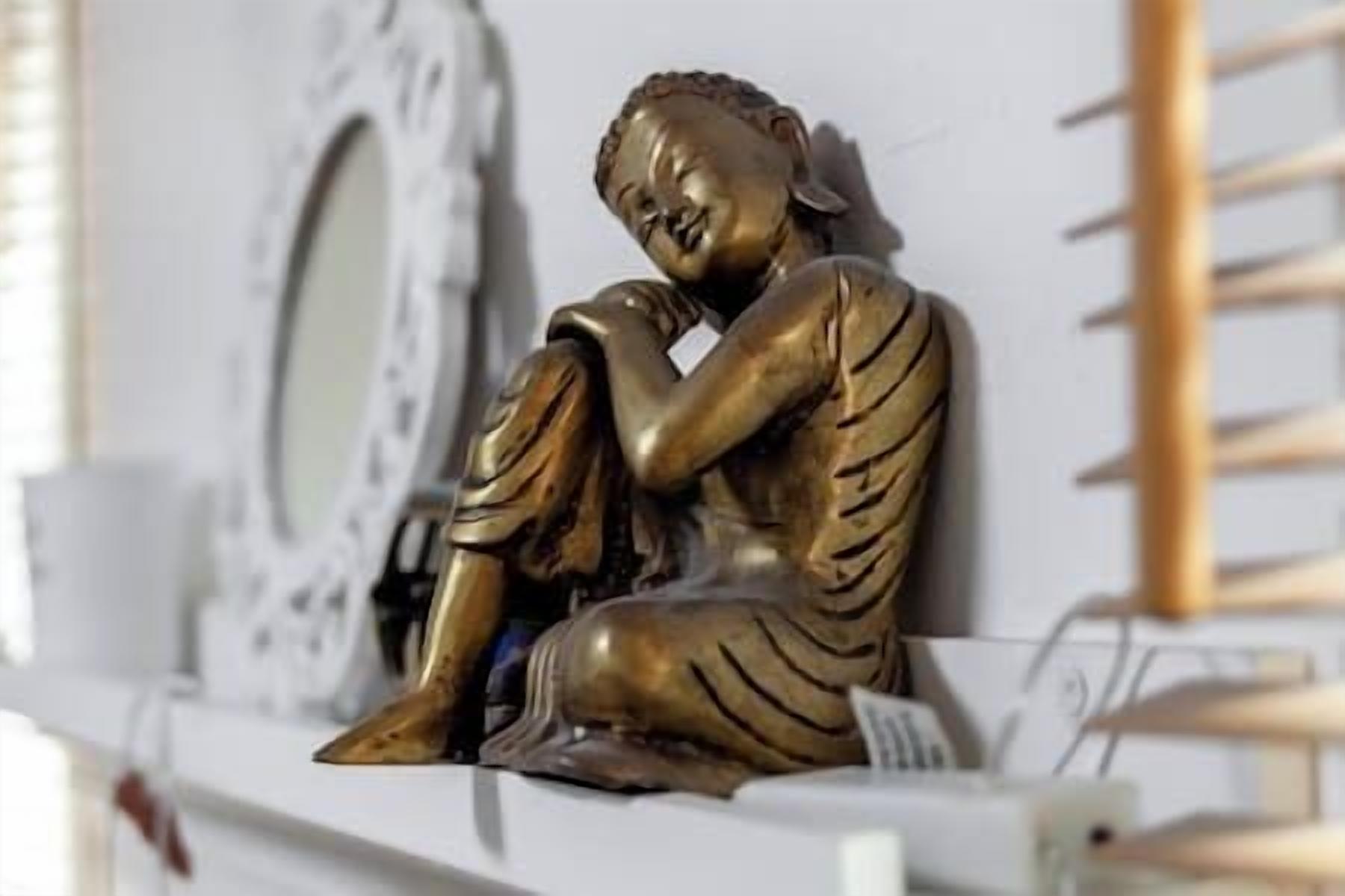 Una estàtua d'una figura asseguda amb una posició contemplativa, col·locada sobre una prestatgeria.