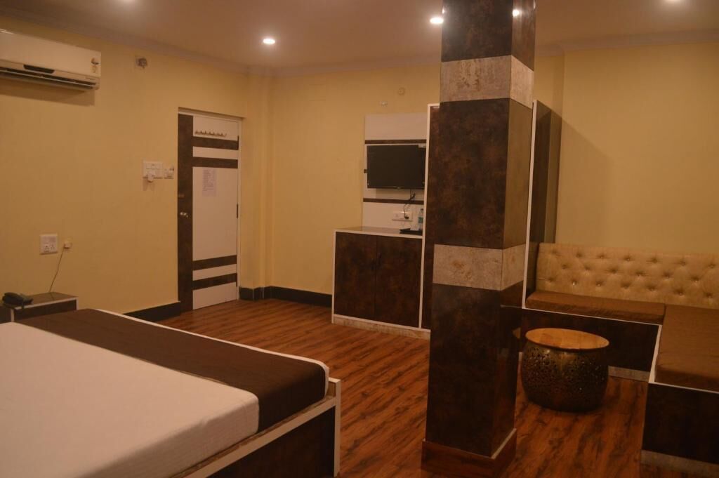 Une chambre d’hôtel avec un lit, une petite table, un canapé, une colonne et un téléviseur.