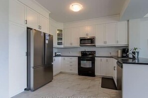 A modern kitchen with white cabinets, stainless steel appliances, and a tiled floor. - Spacious Binbrook Retreat | FREE Parking & Wi-Fi (Hamilton)