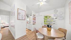 Una cocina moderna con armarios blancos, un comedor con una mesa de madera redonda, sillas de mimbre y un ventilador de techo.