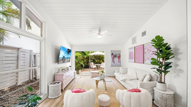Una sala de estar moderna con un sofá blanco, dos sillones blancos, una mesa de centro y un televisor montado en la pared.