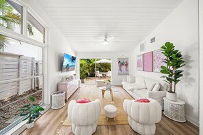 A modern living room with a white sofa, two white armchairs, a coffee table, and a TV mounted on the wall. - Stylish Garden Retreat in Coconut Grove - Pink (Miami)
