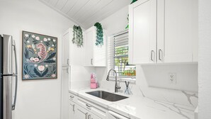 Una cocina moderna con armarios blancos, un refrigerador de acero inoxidable, un lavamanos con grifo y una ventana con persianas.