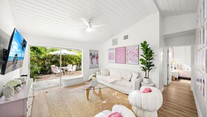 Un salón amplio con un sofá blanco, una mesa de centro y un ventanal con vistas a un jardín tropical.