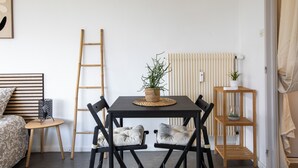 Une pièce comprenant un lit, une table avec des chaises, une petite table d’appoint, une échelle, un radiateur et une étagère avec des plantes.