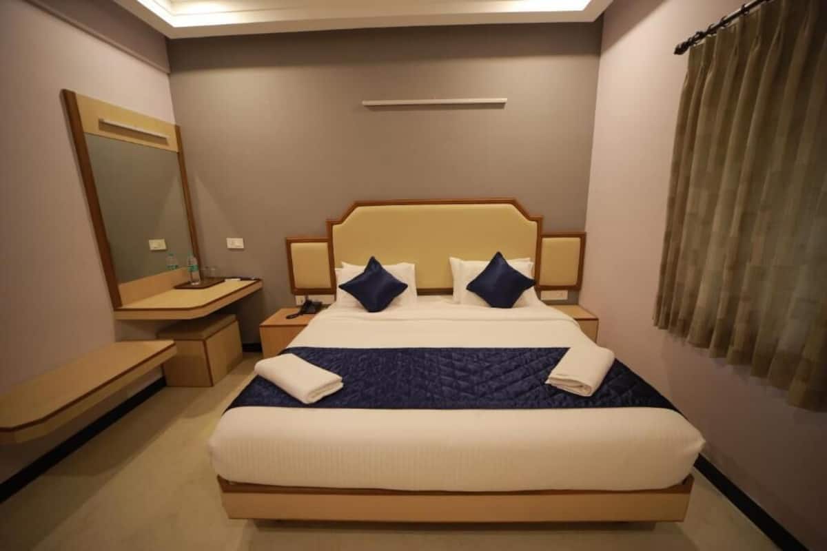 A hotel room with a bed, bedside tables, a mirror, and a window with curtains.