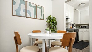 Et spiseområde med et rundt bord og fire træstole, en potteplante og abstrakt kunst på væggen.