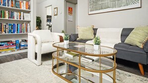 En stue med en hvid sofa, en grå sofa, et glasbord og en reol fyldt med bøger.