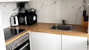 A compact kitchen with white cabinets, a wooden countertop, a built-in oven, a coffee maker, a kettle, and a sink. - Cozy 2BR Apartment Near Meidling Station (Vienna)