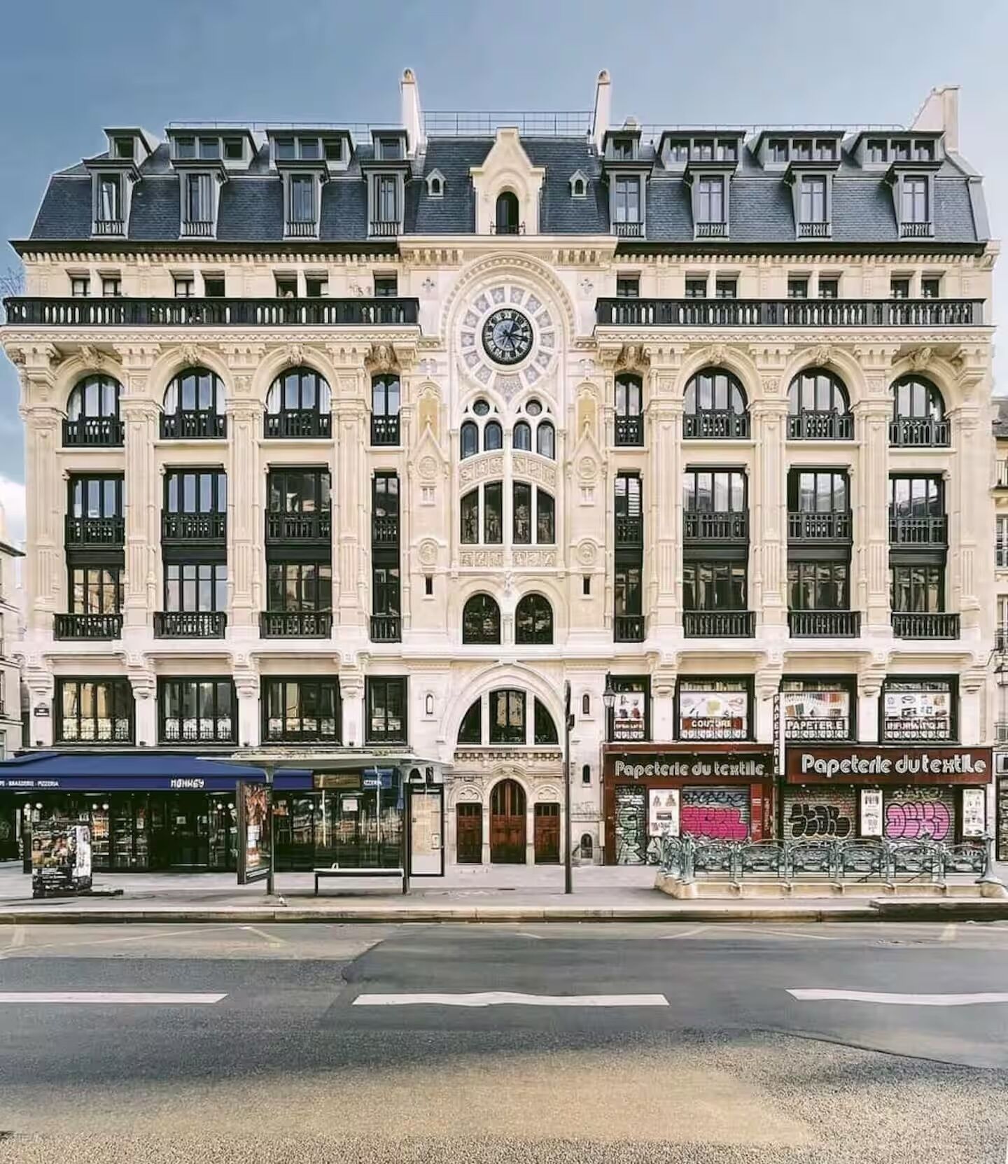 A historic building with a central clock tower, large windows, and a ground-floor shop.